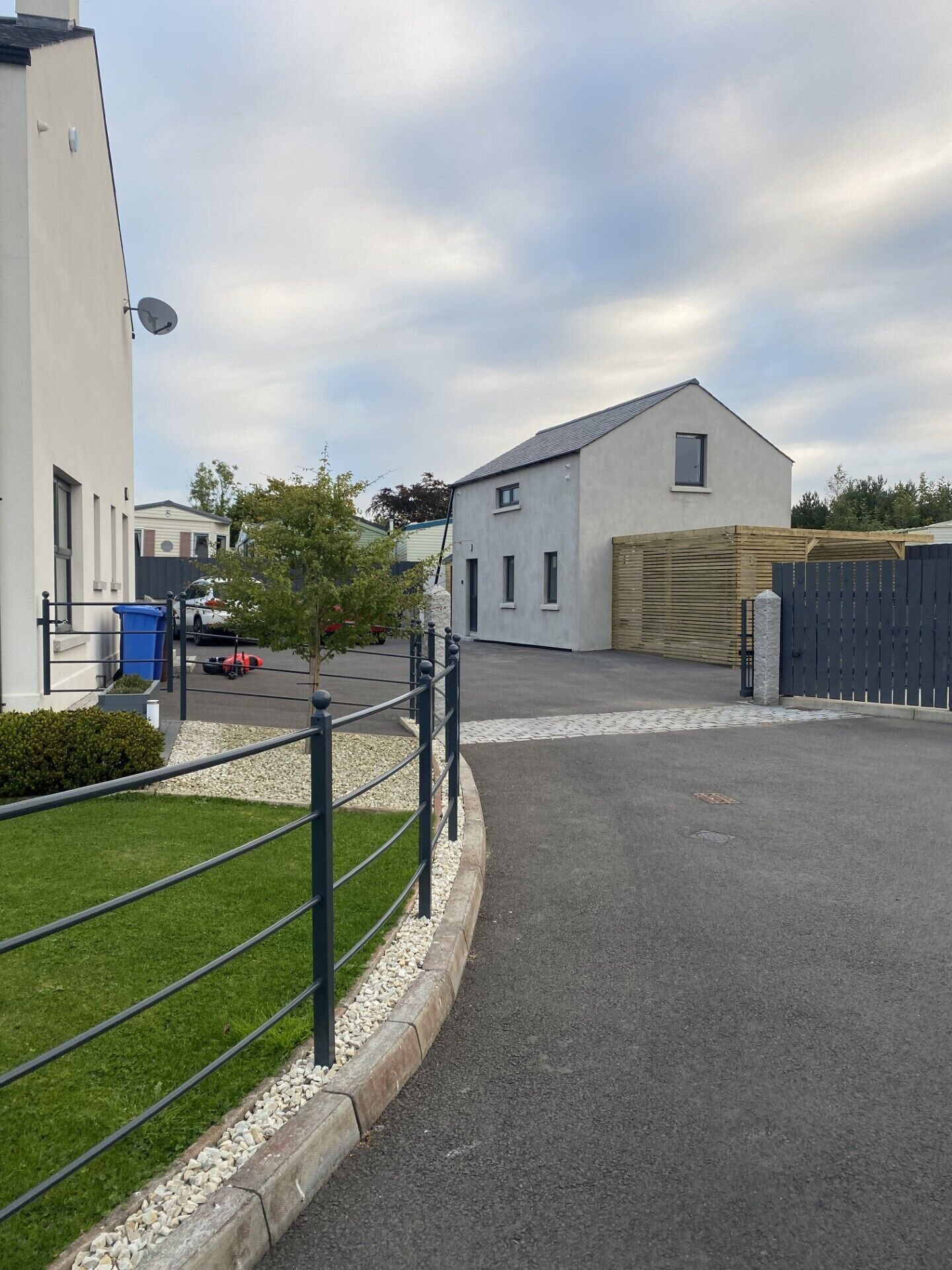 A parking area with a paved road, a metal fence, and a building with a sloped roof.