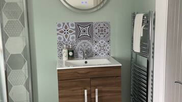 Une salle de bain avec un meuble-lavabo en bois, un miroir rond, un pare-chocs en carreaux à motifs et un porte-serviettes.