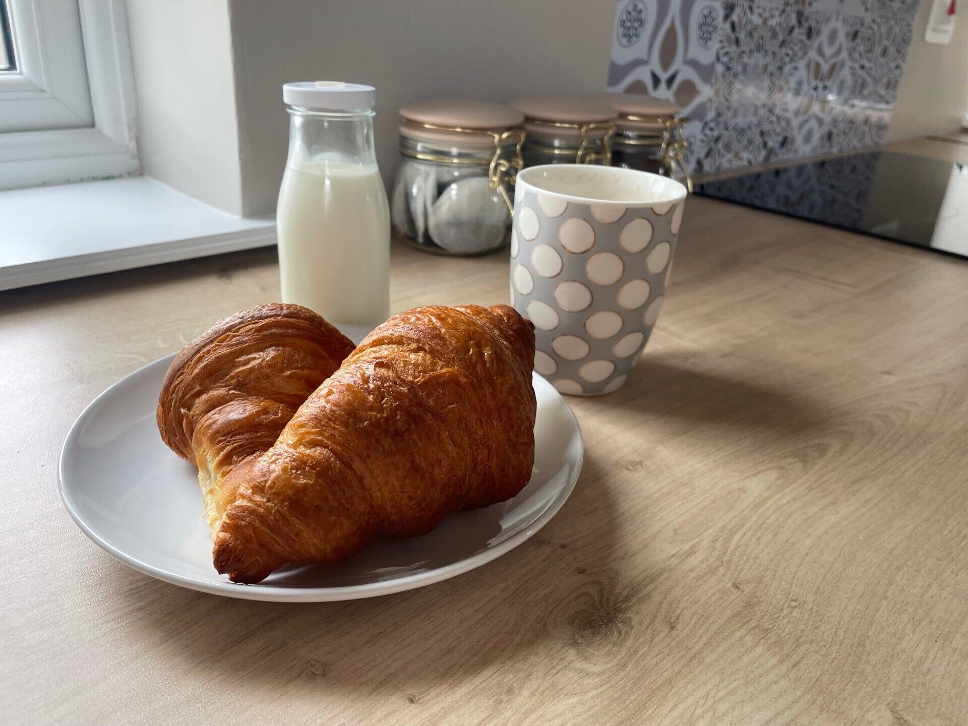 A plate with two croissants and a milk bottle on a wooden table.