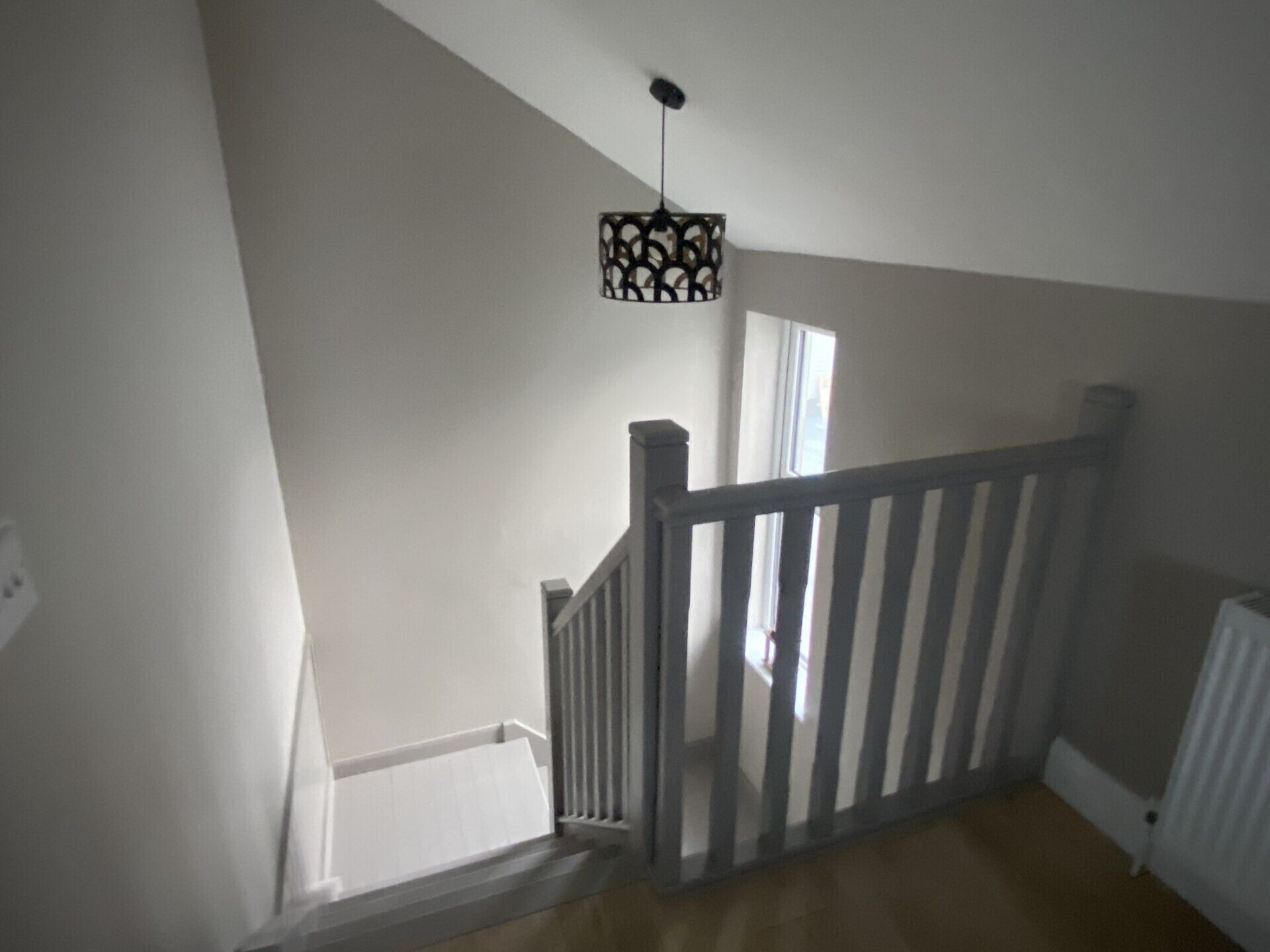 Un escalier avec une rampe blanche et un luminaire suspendu.
