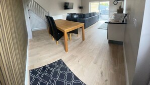 Una sala de estar moderna con una mesa de comedor de madera, sillas negras, un sofá gris y una zona de cocina con encimera y fregadero.