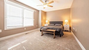 A bedroom with a bed, two bedside tables with lamps, a ceiling fan, and a window with blinds. - 6BR Downtown | Side-by-Side Townhomes | 2 Garages (Indianapolis)