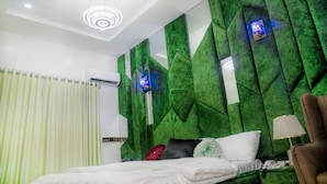 Quarto moderno com parede verde texturizada, cama com roupa de cama branca, poltrona marrom e luminária de teto.