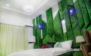 Quarto moderno com parede verde texturizada, cama com roupa de cama branca, poltrona marrom e luminária de teto.