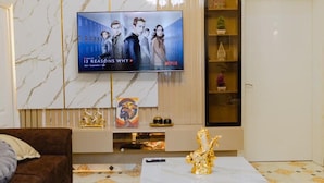 Uma sala de estar com parede de mármore, televisão na parede, sofá marrom, mesa de centro e uma prateleira decorativa com objetos pequenos.