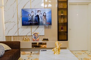 Uma sala de estar com parede de mármore, televisão na parede, sofá marrom, mesa de centro e uma prateleira decorativa com objetos pequenos.
