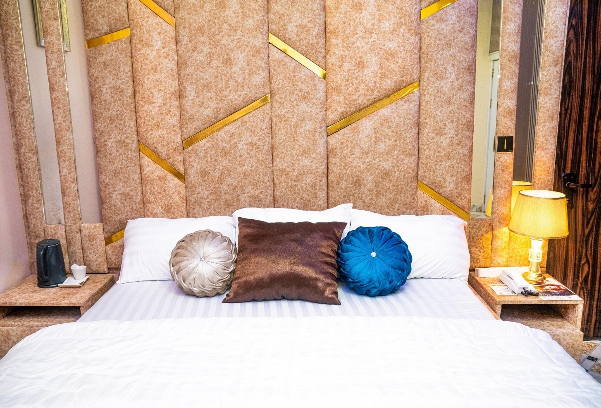 A hotel room with a bed, pillows, a nightstand, a lamp, and a wall with a geometric pattern.