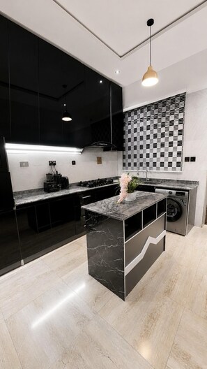 A modern kitchen with a central island, black cabinets, and a checkered backsplash. - Luxury Apartment Fast Wifi - 24/7 Power (Abuja)