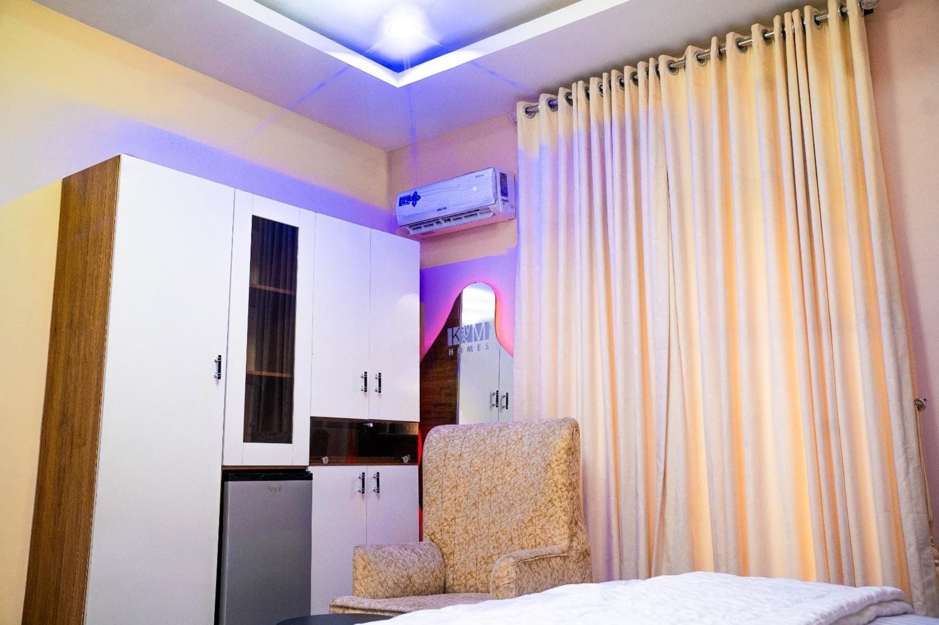Un dormitorio con cama, una silla, armario y aire acondicionado.
