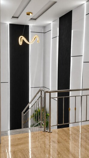 A modern interior with a polished marble floor, a staircase with metal railings, and a unique wall-mounted light fixture. - Luxury Apartment Fast Wifi - 24/7 Power (Abuja)