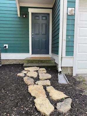 A house with a dark blue door, a stone pathway leading to the front steps, and a white garage door.