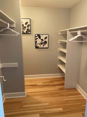 A walk-in closet with wooden flooring, white shelving units, and two framed leaf artworks on the wall.
