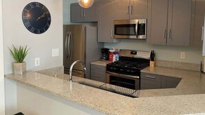 Uma cozinha moderna com armários cinza, eletrodomésticos de aço inoxidável, bancada de granito e um relógio na parede.