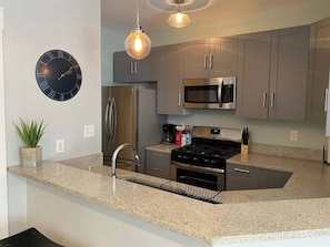 A modern kitchen with grey cabinets, stainless steel appliances, a granite countertop, and a wall clock.