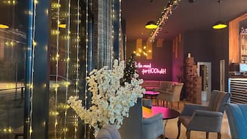 Un espace lounge moderne doté d’une grande fenêtre décorée de guirlandes lumineuses, d’un coin salon avec des canapés et des tables, et d’un néon en arrière-plan.
