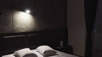 A dimly lit bedroom with a bed, a nightstand, and a wall-mounted light fixture.
