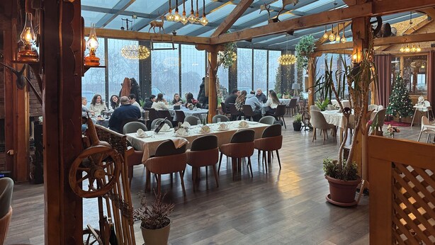 A restaurant with a high ceiling and large windows, wooden beams, and hanging light fixtures. - Antika Hotel (Pec)