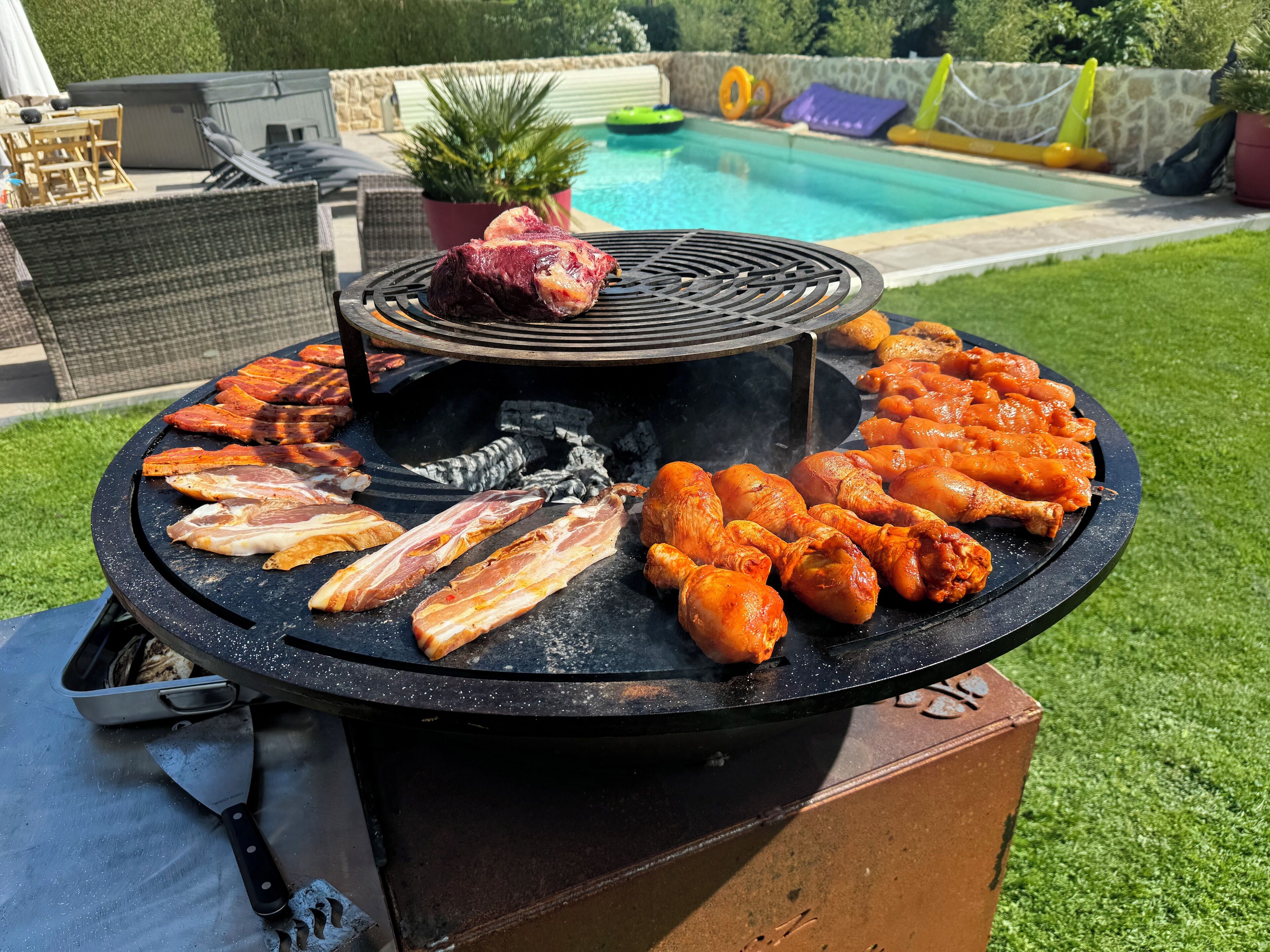 A barbecue grill with various meats cooking outdoors.