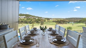 A dining table set for six with a scenic view of a golf course and hills in the background.