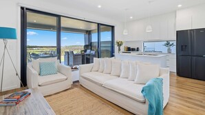 A modern living room with a white sofa, a coffee table with books, and a view of the outdoors.