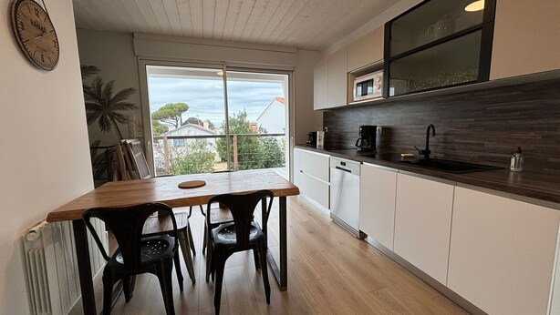 A modern kitchen with a wooden table and chairs, a built-in oven, and a view of the outdoors.