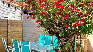 A patio with a table and chairs, surrounded by a wooden fence and a tree with red flowers.