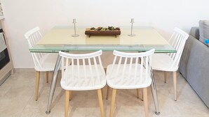A dining area with a glass-top table, four white chairs with wooden legs, and a small plant on the table. - Charming 1-bedroom apartment in delightful Chios and traditional Kampos area.  (Chios)