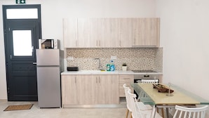 A compact kitchen with a microwave, refrigerator, and a small dining area with a glass table and white chairs. - Charming 1-bedroom apartment in delightful Chios and traditional Kampos area.  (Chios)