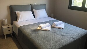 A neatly made bed with a grey quilt, white pillows, and two rolled towels on the bed. - Charming 1-bedroom apartment in delightful Chios and traditional Kampos area.  (Chios)
