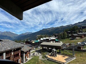 A mountain village with traditional wooden buildings, a playground, and a ski lift.