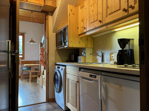 A compact kitchen with wooden cabinets, a washing machine, a dishwasher, a microwave, and a coffee maker.