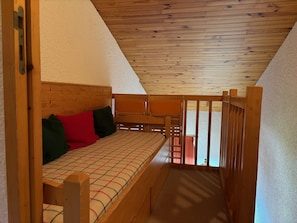 A cozy attic bedroom with a wooden bunk bed, a small table, and a view of the outside.