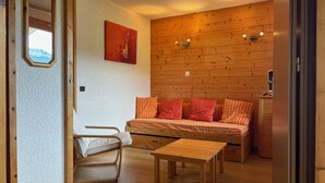 Een knus vertrek met een houten wand, een bed met rode kussens, een houten tafel en een spiegel aan de linkerkant.