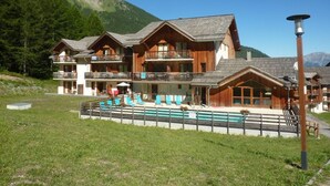 A multi-story wooden chalet with balconies, a swimming pool, and a mountain backdrop. - Modern 2-room apartment for 6 people with pool, sauna, hammam, wifi and pets allowed (Les Orres)
