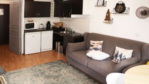 A compact living space with a kitchenette, a gray sofa with decorative pillows, and a patterned rug. - Modern 2-room apartment for 6 people with pool, sauna, hammam, wifi and pets allowed (Les Orres)