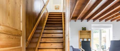 A wooden staircase leading to a living area with a sofa, chairs, and a bookshelf.