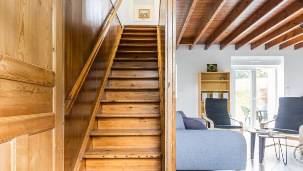 A wooden staircase leading to a living area with a sofa, chairs, and a bookshelf. - Restored 19th Century Semi-detached House in Normandy (Saint-Joseph (Manche))