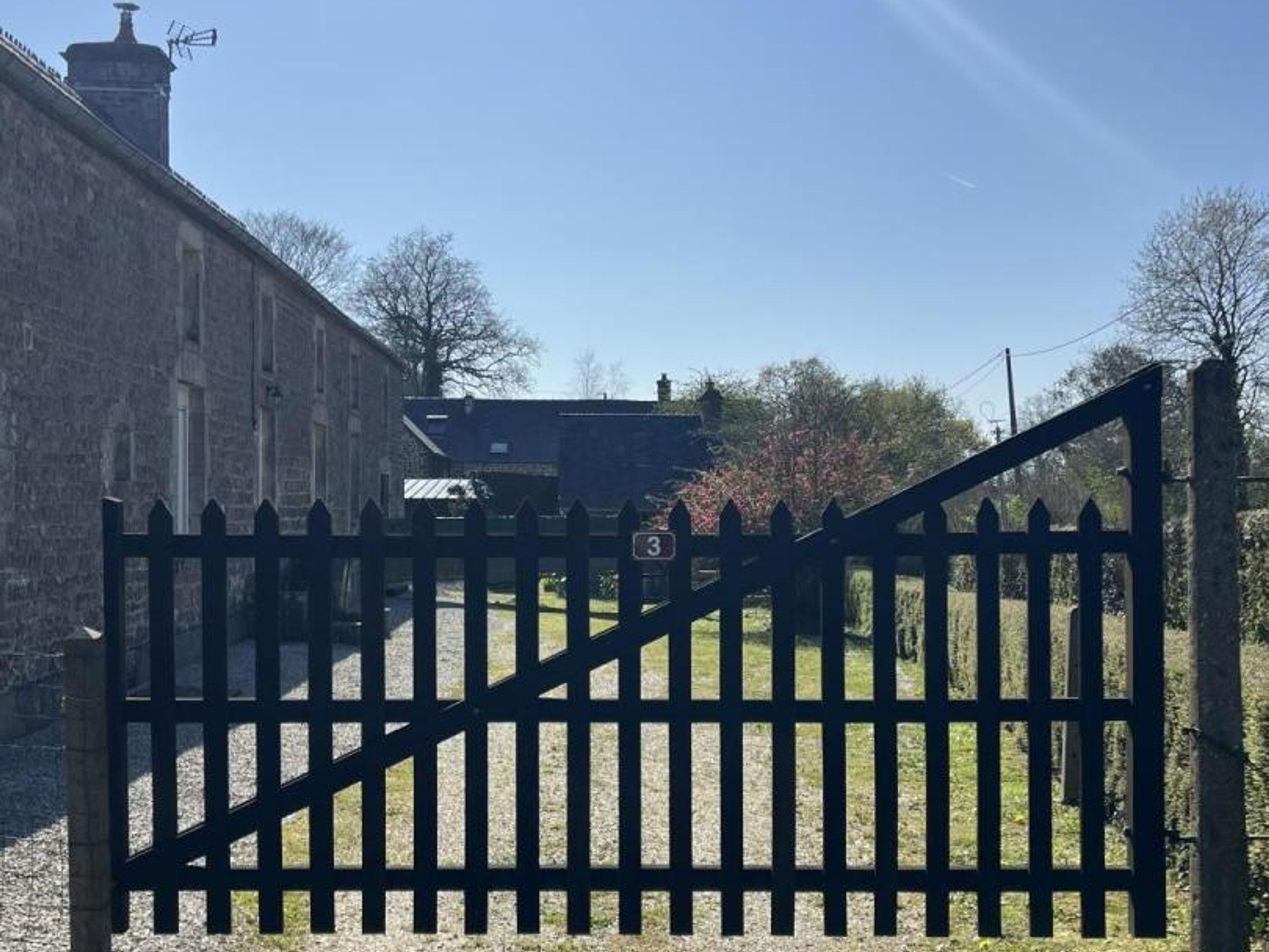 A gated entrance with a number 3 sign, a stone building, and a clear sky.