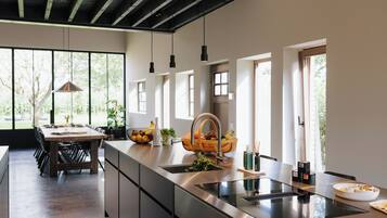 Een moderne keuken met een groot eiland, roestvrijstalen apparatuur en een eethoek met een houten tafel en stoelen.