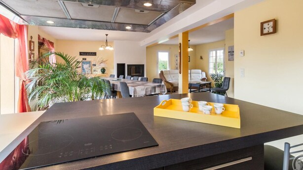 A modern kitchen with a built-in stove, dining area with chairs, and a yellow accent wall. - Spacious house with enclosed garden in Yvetot-Bocage (Yvetot-Bocage)