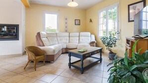 A living room with a sectional sofa, a wicker chair, a coffee table, and a potted plant. - Spacious house with enclosed garden in Yvetot-Bocage (Yvetot-Bocage)