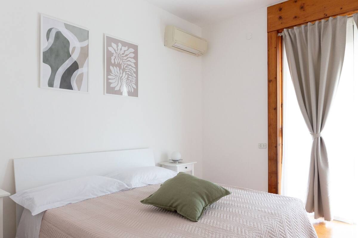 Een slaapkamer met een bed, kussens, een nachtkastje en wanddecoratie.