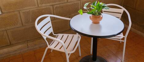 A small round table with a potted plant, two white chairs, and a tiled floor.