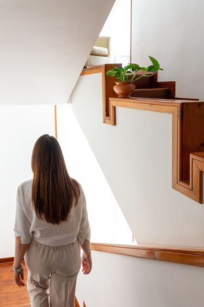 A woman walking up a wooden staircase with a potted plant on the landing. - B&B Le foglie d'ulivo (Bari)