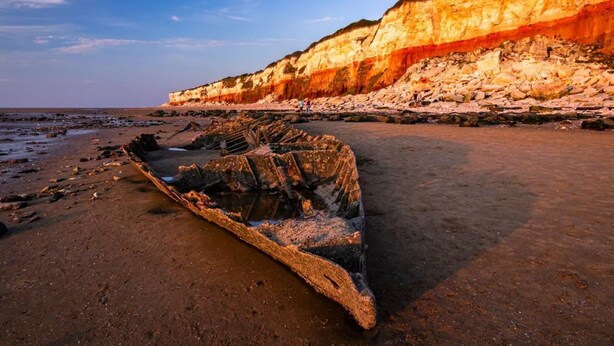 A coastal landscape with a large cliff and a shipwreck on the beach. - Place2bee , Caravan , Manor park , Free Wifi ,6 Berth (Hunstanton)