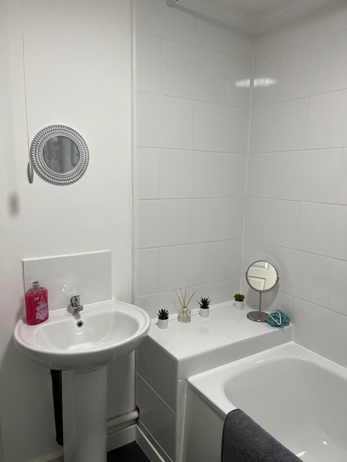 Une salle de bain avec un lavabo blanc, un miroir, une petite plante en pot et une baignoire.