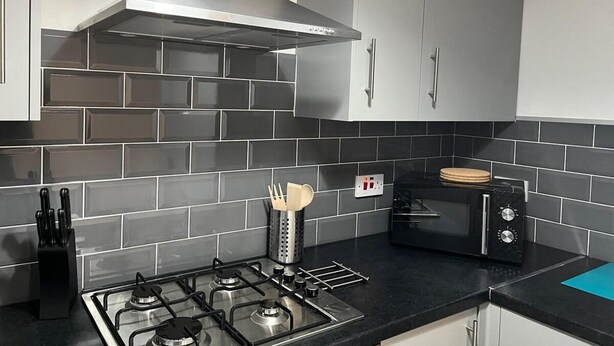 Una cocina moderna con gabinetes grises, una estufa a gas, horno empotrado y microondas.
