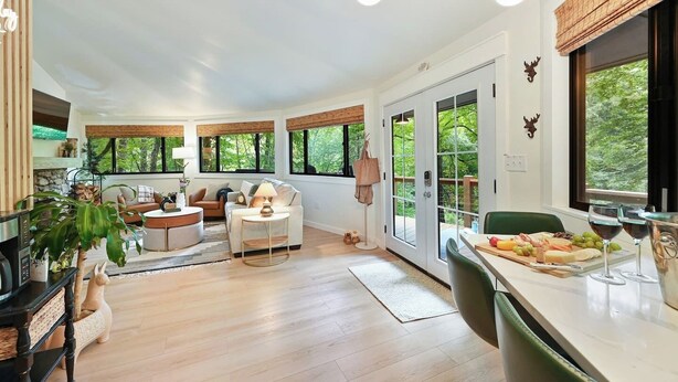 A spacious living area with a fireplace, a dining table set with a fruit platter and wine glasses, and large windows offering a view of greenery. - Luxury tree house-like accommodations in the Blue Ridge Mountains. Ski/bike/hike (Mars Hill)