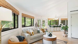 A spacious living room with a sofa, armchair, and round coffee table. A kitchen with bar stools is visible in the background. - Luxury tree house-like accommodations in the Blue Ridge Mountains. Ski/bike/hike (Mars Hill)