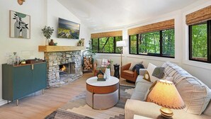 A spacious living room with a stone fireplace, a comfortable sofa, a coffee table, and large windows offering a view of the outdoors. - Luxury tree house-like accommodations in the Blue Ridge Mountains. Ski/bike/hike (Mars Hill)